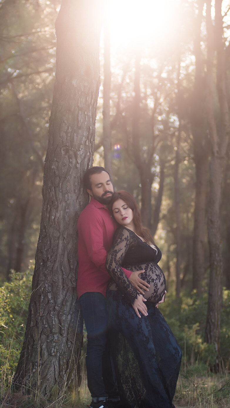 Fotografía de embarazada con su pareja en el bosque apoyados en un pino