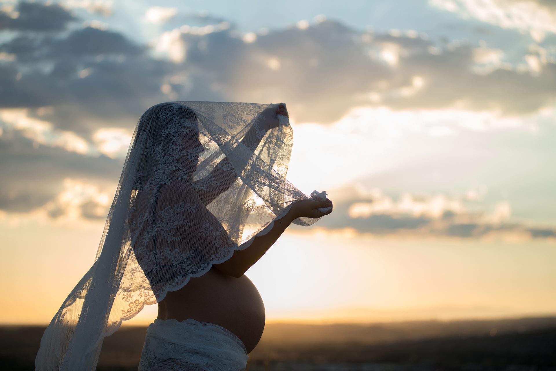 Fotografía de mujer embarazada con camisón blanco en el campo al atardecer