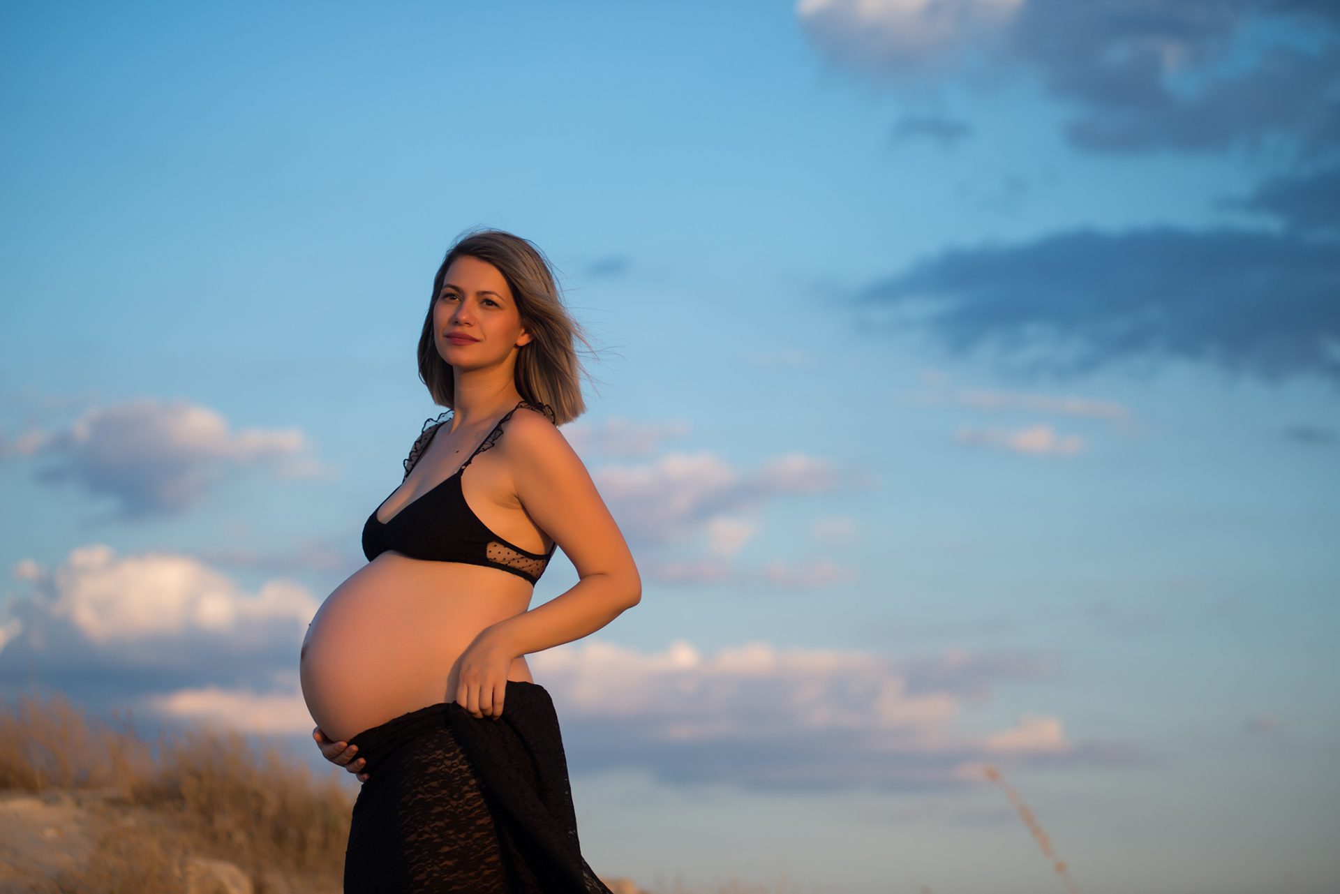 Fotografía de mujer embarazada con traje de baño negro en el campo al atardecer